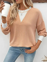 A peach-colored two-tone ribbed knit sweatshirt with a white v-neckline, slightly stretchy fabric, and exposed seam details