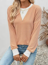 A soft peach-colored slightly stretchy ribbed knit sweatshirt with white v-neck and cuffs featuring exposed seam details