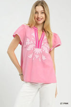 A light pink short-sleeved Umgee top with white abstract applique split neck and embroidered floral patterns