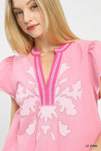 Umgee light pink short-sleeved top with abstract applique split neck, white embroidered florals, and lace trim neckline