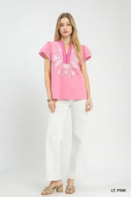 A light pink Umgee short-sleeved top with white floral abstract applique and a v-neck split neck design