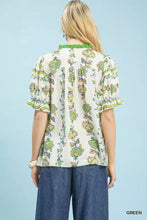 Woman wearing an off-white umgee abstract border print blouse with green and yellow floral pattern and ruffled sleeves