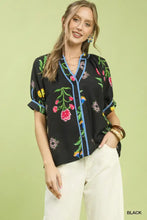 Black short-sleeved Umgee blouse with vibrant botanical print contrast and blue contrast trim button detail