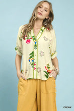Cream-colored umgee botanical print blouse with embroidered floral design green trim and short sleeves