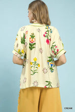 Cream-colored umgee botanical print blouse with vibrant pink yellow and green embroidered floral patterns on soft fabric