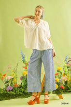 A woman wears a cream-colored Umgee cotton gauze ruffle top with short sleeves and pleated details