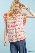 A woman wears an umgee double frill tangerine blouse with floral geometric pattern and short flutter sleeves