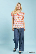 A woman wears an umgee double frill tangerine blouse with floral geometric pattern and short flutter double frill sleeves