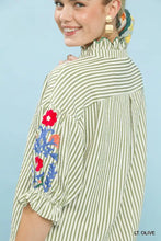 A woman wears an umgee embroidered ruffle trim stripe blouse with light olive and white stripes and floral embroidery