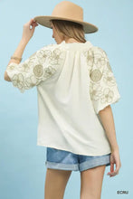 Cream-colored umgee embroidered blouse features floral embroidery on puffed short sleeves and a loose boho fit