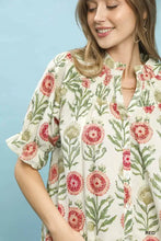 A woman wears an Umgee button-front short sleeve top with cream floral pattern and ruffled sleeves