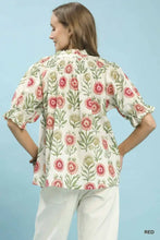 A woman wears an umgee floral button-front short sleeve top in cream with pink and green blossoms and ruffled sleeves