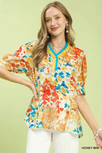 Umgee floral contrast pleat neck top with vibrant floral print, yellow and blue v-neck collar, and short puffed sleeves on off-white base