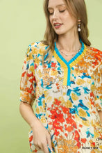 Umgee floral contrast pleat neck top featuring a cream base with bold orange and blue floral print and yellow v-neckline