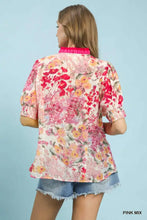 A woman wearing an umgee floral contrast pleat neck top in pink with vibrant floral print and ruffled short puffed sleeves