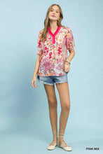 A woman wears an umgee floral contrast pleat neck top with pink and white floral print and bright pink v-neckline