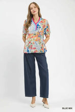 A woman wears an Umgee floral contrast pleat neck blouse with vibrant floral print and navy wide-leg trousers