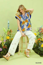 A woman wears an umgee floral print blouse with vibrant blue orange white floral print and contrast trim and v neckline