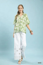 A woman wearing an Umgee floral print sage green and white puff sleeve blouse with a high low curved hem