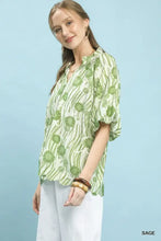 A woman wears an umgee floral print scalloped edge blouse in sage green and white with puff sleeves and high-low hem