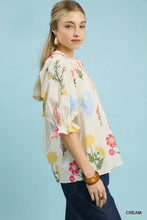 Cream-colored umgee floral split neck puff sleeve top with pink yellow and blue flowers on an off-white background