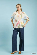 Cream-colored umgee floral split neck puff sleeve top with embroidered pink blue and green floral patterns on soft fabric