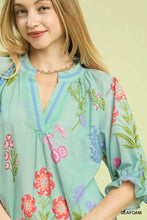 A light seafoam green umgee floral split neck puff sleeve top with vibrant pink red and purple blossoms on soft fabric
