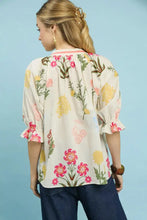 A woman wears an Umgee floral split neck puff sleeve top in cream with vibrant pink and yellow floral patterns