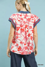 A woman wears an umgee floral split neck top with vibrant red pink floral print and navy trim on short-sleeved blouse