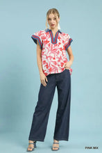 A woman wears an umgee floral split neck top with vibrant pink and red floral split pattern and navy blue trim