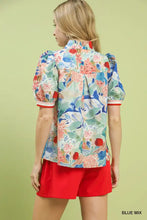 A vibrant blue umgee jacquard bloomscape floral print blouse with puff sleeves and red-trimmed cuffs