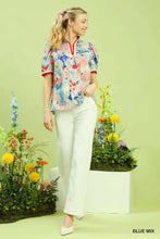 A woman wears a vibrant blue floral print umgee jacquard bloomscape top with short puffed sleeves and red trim