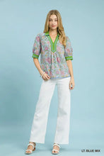 A woman wears a light blue umgee mix floral puff sleeve blouse with green contrast trim and short sleeves