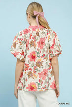 A women’s coral umgee mix floral print blouse with puff sleeves and a pink ribbon tie at the neckline