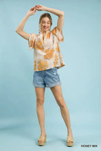 A woman wears an umgee mix floral ruffle sleeve blouse in light fabric with orange and yellow floral patterns
