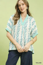 Women’s short-sleeved mix print boho blouse in teal and white floral with chevron-trimmed collar and cuffs by umgee