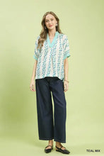A woman wears a teal and white umgee mix print boho blouse with contrast trim and v-neckline short sleeves