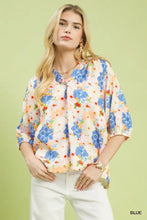 A woman wearing an umgee mixed floral print blouse in blue and peach with three-quarter sleeves