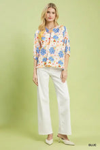 A woman wearing an umgee mixed floral print blouse in blue with three-quarter sleeves and white wide-leg pants