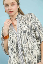 A woman wearing a cream mixed print button front top with black botanical illustrations and striped trim by umgee
