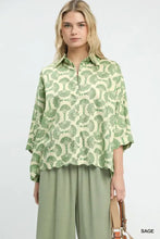 A woman wears an Umgee printed button down shirt in sage green and cream with fan-shaped motifs and flared sleeves