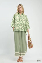 A woman wears a sage green umgee printed button down shirt with white embroidery and matching wide-leg pants