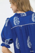 A vibrant royal blue umgee printed puff sleeve split neck top with intricate white embroidered botanical patterns and collar trim
