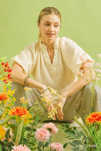 A woman wears a cream-colored umgee scalloped hem textured blouse with short sleeves and a gathered neckline