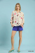 A woman wears a light-colored umgee button-down top with a coral and pink starfish print and seashell design
