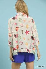 A woman wears an umgee cream blouse with a vibrant coral starfish print in reds pinks greens and purples