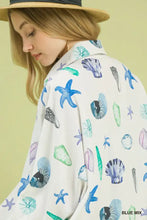 White blouse with vibrant blue green and purple starfish print featuring seashells on a light background by umgee