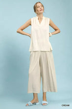 Cream-colored umgee sleeveless textured notch neck top with vertical pleats and relaxed flowing silhouette