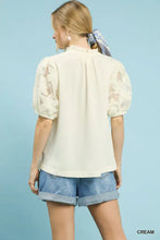 Cream-colored umgee blouse features puff sleeves textured fabric floral lace insets and a ruffled neckline