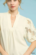 Cream-colored Umgee blouse featuring textured fabric, ruffled neckline, and puff sleeves with floral lace detailing